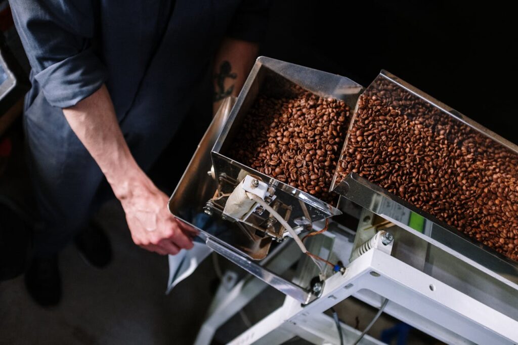 Close-up of coffee beans being sorted by a worker in an industrial machine.